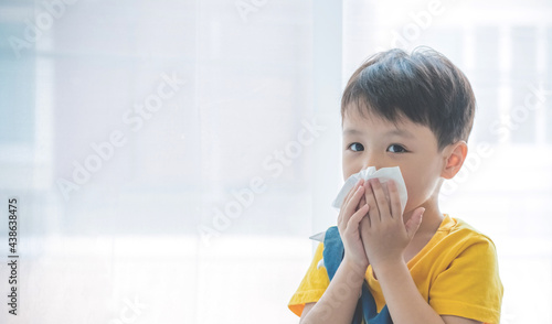 Little boy blowing nose into tissue paper and wearing surgical face mask. Copy space.