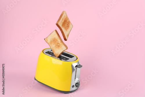 Tableau sur toile Bread slices popping up from modern toaster on pink background