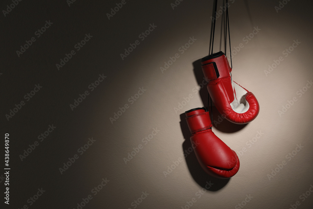 Pair of boxing gloves hanging on beige wall, space for text