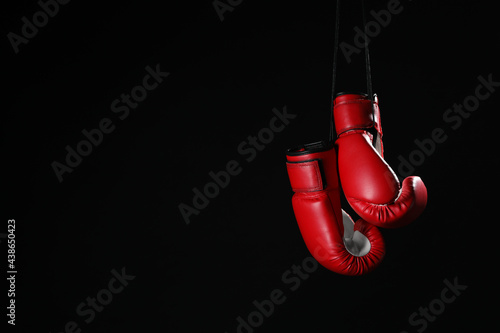 Pair of red boxing gloves hanging on black background, space for text