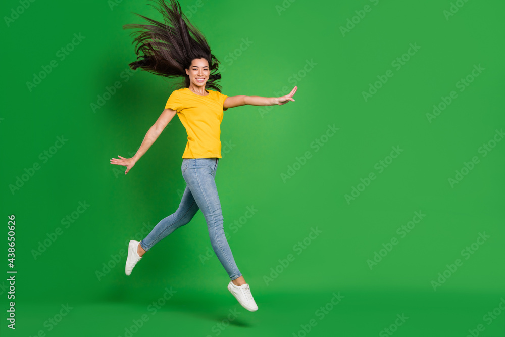 Full size photo of attractive pretty young woman jump up walk smile fly hair isolated on green color background Full size photo of attractive pretty young woman jump up walk smile fly hair isolated on green color background