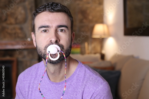 Fotografie Spoiled grown up man licking a pacifier to control a tantrum