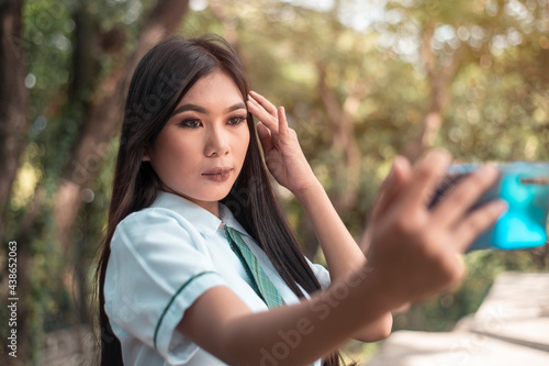 Canvas Print A pretty vain young asian woman in a student uniform takes a selfie of herself while outdoors