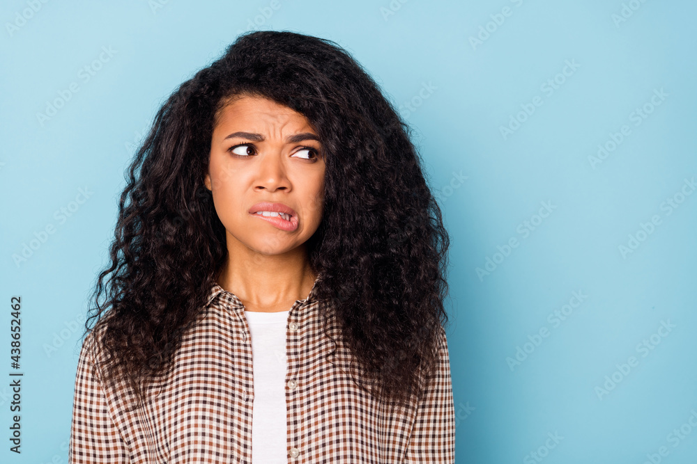 Photo of stressed wavy hairdo young lady bite lip look empty space wear brown shirt isolated on vivid blue color background Photo of stressed wavy hairdo young lady bite lip look empty space wear brown shirt isolated on vivid blue color background