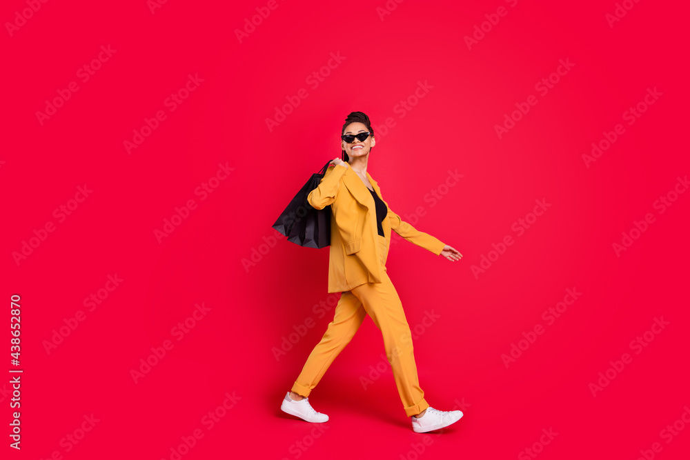 Profile full body photo of cute lady go with bags wear yellow blazer isolated on vivid red color background Profile full body photo of cute lady go with bags wear yellow blazer isolated on vivid red color background
