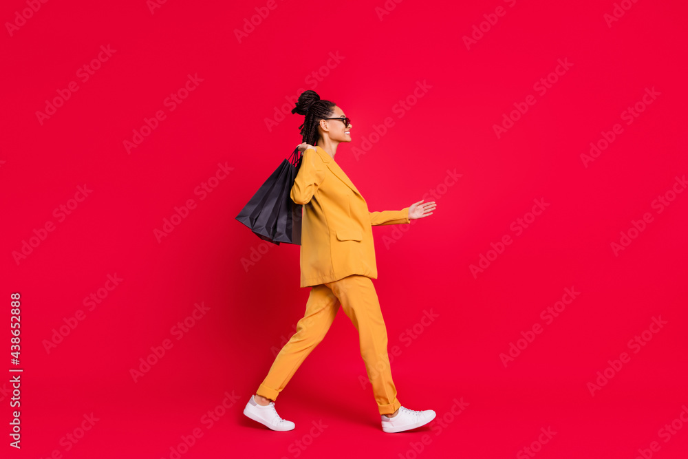 Profile full length photo of nice lady go shake hand with bags wear yellow blazer isolated on vivid red color background Profile full length photo of nice lady go shake hand with bags wear yellow blazer isolated on vivid red color background