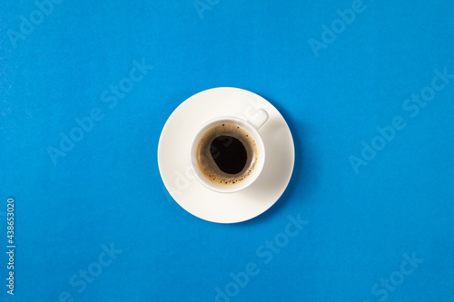 Flat lay of cup of coffee on blue background with copy space