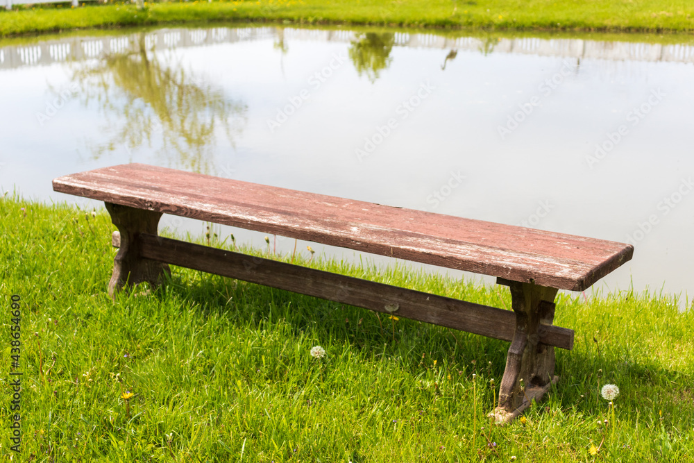 Fototapeta premium Red bench with a tree by the shore of a lake in spring