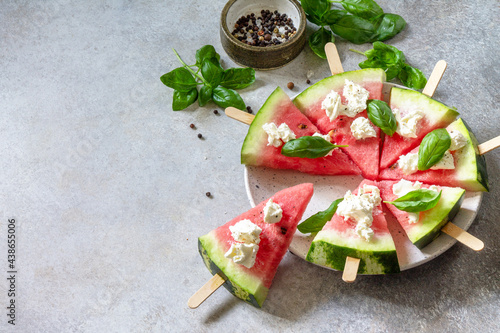 Healthy seasonal dieting and nutrition, summer snack. Watermelon pizza with feta cheese and basil on a gray stone tabletop. Copy space.