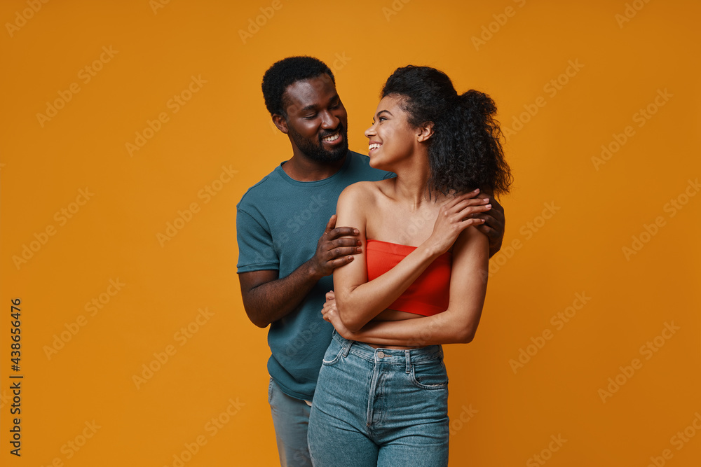 Beautiful young African couple smiling and embracing while standing against yellow background Beautiful young African couple smiling and embracing while standing against yellow background
