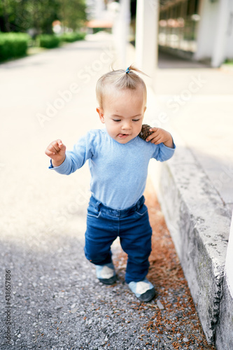 Little girl with a ponytail walks along the road in the park and carries a pebble on her shoulder