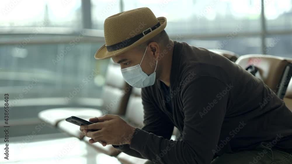 Young traveler man wearing mask protect flu coronavirus. Tourist in airport terminal using smartphone sitting and waiting his flight. During the pandemic must be social distancing self quarantine. Young traveler man wearing mask protect flu coronavirus. Tourist in airport terminal using smartphone sitting and waiting his flight. During the pandemic must be social distancing self quarantine.