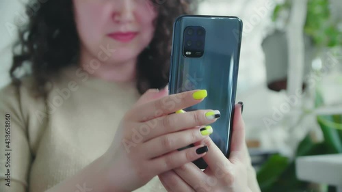 Young cheerful curly girl flips the phone and smiles sitting at the table in the restaurant