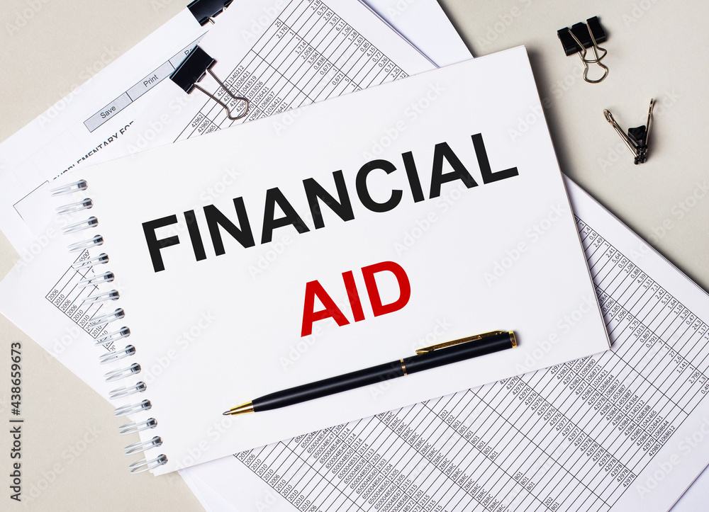 On the desktop there are documents, pen, black paper clips and a notebook with the text FINANCIAL AID. Business concept On the desktop there are documents, pen, black paper clips and a notebook with the text FINANCIAL AID. Business concept
