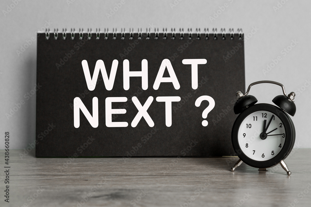 text WHAT NEXT . black notebook and CLOCK on desk background. text WHAT NEXT . black notebook and CLOCK on desk background.