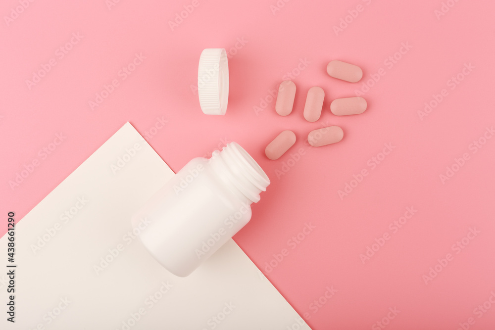 Creative flat lay with nutritional supplement or vitamins for woman. Vitamins for nail and hair growth or supplement for beautiful skin. Opened medication bottle with spilled pink pills on pink backgr Creative flat lay with nutritional supplement or vitamins for woman. Vitamins for nail and hair growth or supplement for beautiful skin. Opened medication bottle with spilled pink pills on pink backgr