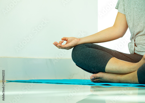 Close up mudra hand of Asian young woman sitting and practices yoga breathing meditation pose on blue mat near window of gym with copy space