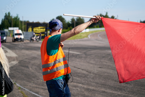 Photography A marshal at a racetrack holds up a red flag to the rider(s).