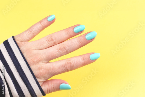 Female hand in sailor striped shirt with beautiful manicure - mint blue nails on yellow background