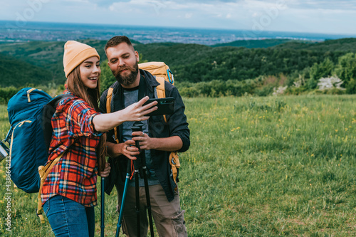 A young couple of hikers taking selfie with a smartphone and using trekking poles