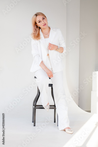 Confident young beautiful manager on white background. blonde girl in a white suit sits on a chair, on a white background. Strong and independent businesswoman.