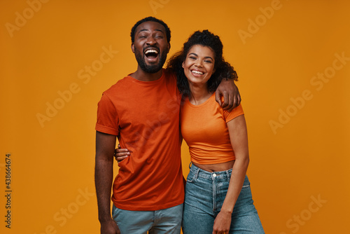 Beautiful young African couple looking at camera and smiling while standing against yellow background