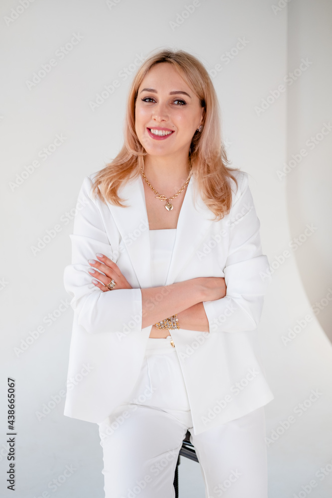 Confident young beautiful manager on white background. blonde girl in a white suit sits on a chair, on a white background. Strong and independent businesswoman. Confident young beautiful manager on white background. blonde girl in a white suit sits on a chair, on a white background. Strong and independent businesswoman.