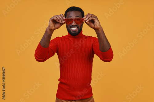 Handsome young African man in casual clothing looking at camera and adjusting eyeglasses