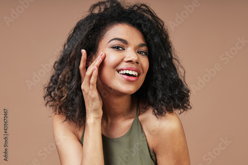 Beautiful young African woman in casual clothing touching her face and smiling