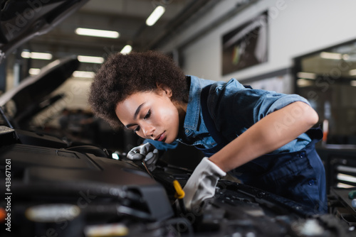 young african american mechanic fixing motor in car with open hood in garage