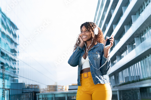 Happy young woman listening music with smart phone in the street with colorful pants