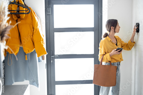 Woman enters a code on the alarm keyboard at the hallway indoors. Concept of home security and smart alarm. Businesswoman coming or leaving home photo