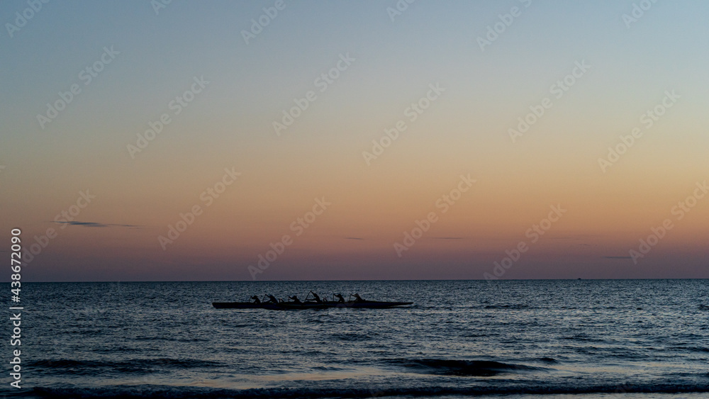 Rowing crew in silhouette on water against pastel sunset sky Rowing crew in silhouette on water against pastel sunset sky