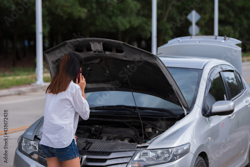 Young woman using mobile phone while looking at broken down car on street. © phonix_a