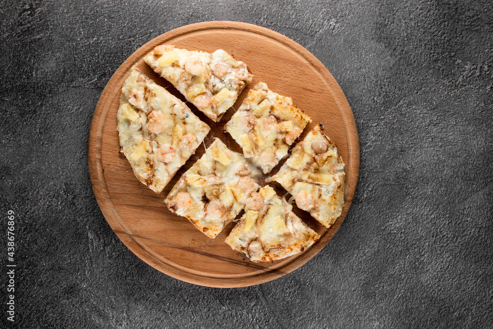 Pinsa romana with shrimps and pineapple on wooden plate on dark background. Seafood scrocchiarella. Pinsa romana with shrimps and pineapple on wooden plate on dark background. Seafood scrocchiarella.