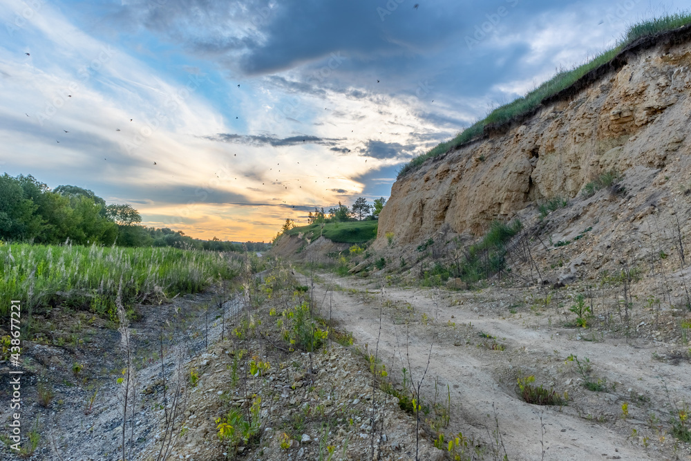 sunset landscape with a steep hill, country road and a flock of swifts in the air sunset landscape with a steep hill, country road and a flock of swifts in the air