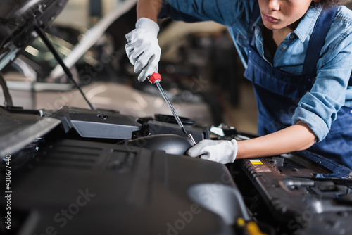partial view of young african american mechanic holding screwdriver and fixing car motor in garage