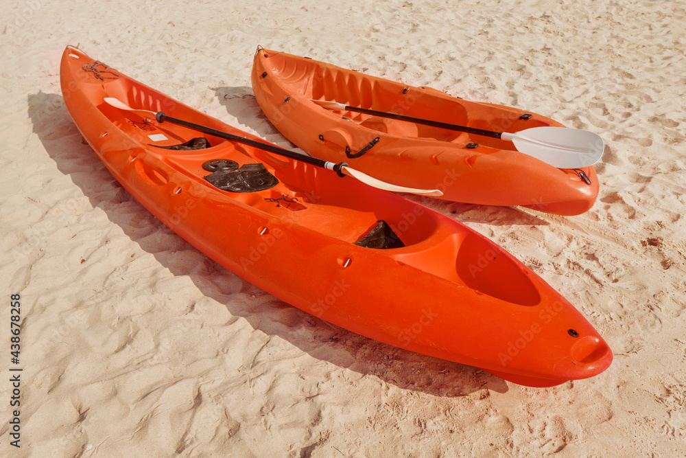 Red canoe and kayak with paddles lie on a sandy beach on a tropical island, waiting for adventurers and tourists to explore the coastal area. Red canoe and kayak with paddles lie on a sandy beach on a tropical island, waiting for adventurers and tourists to explore the coastal area.