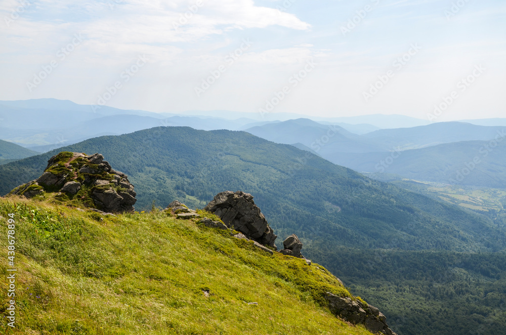 Fototapeta premium Green grass and rocky slope on Pikuj mountain peak at summer time, forest slopes on background. Carpathian Mountains, Ukraine.
