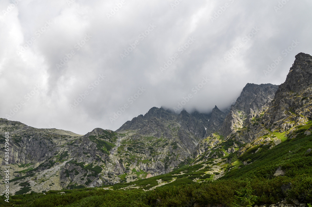 Obraz premium Landscape with high stone sharp rocky peaks under cloudy sky in National Park High Tatras Mountains, Slovakia. Tourist destination for hiking and tourism