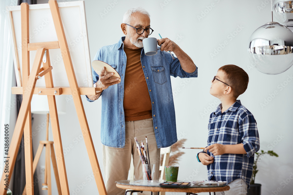 Grandfather and grandson talking while painting on canvas at home workshop.