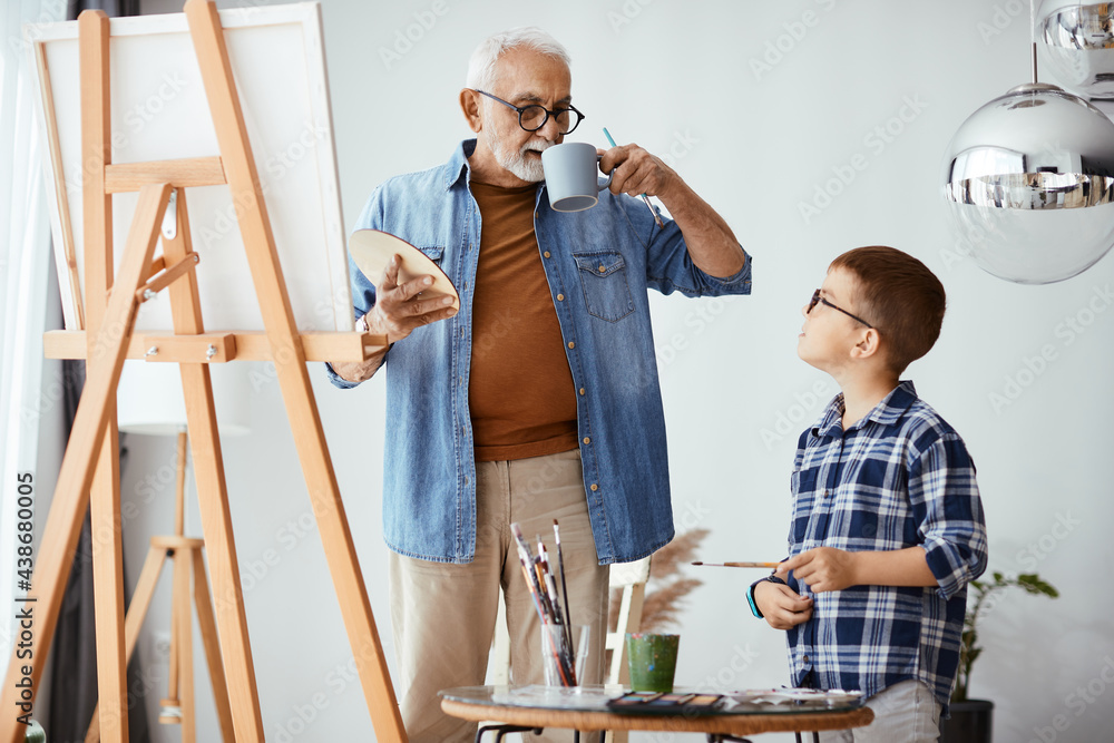 Grandfather and grandson talking while painting on canvas at home workshop. Grandfather and grandson talking while painting on canvas at home workshop.