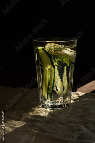 Glass of water with lemon, herbs and cucumber on black background. Vertical.