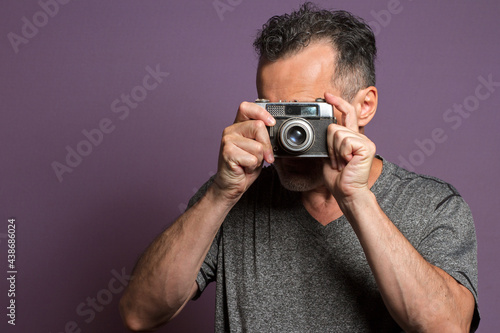 Portrait of a professional photographer isolated on a purple background taking a picture with a vintage camera.
