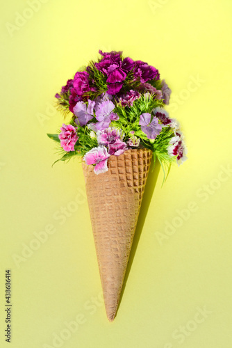 Still life with an ice cream cone, on a yellow background. In the bag there are many colorful flowers, so-called mustaches, which are in the waffle instead of the ice cream