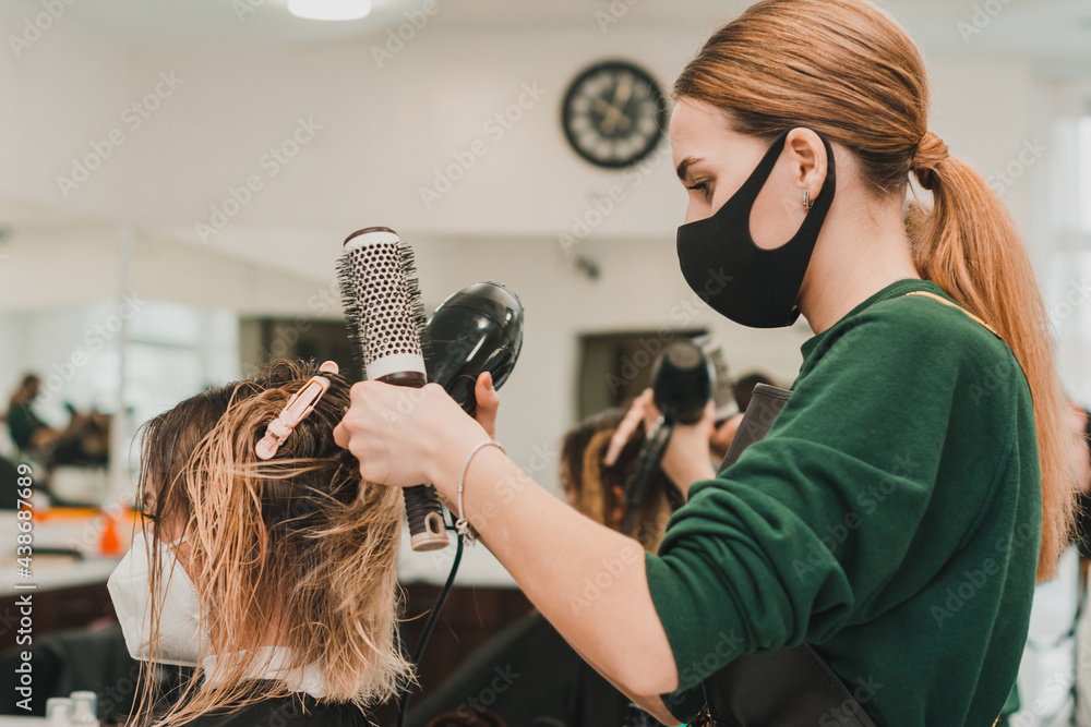 Hairdresser in a mask with at work, drying hair in a client