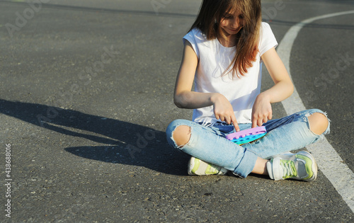 Girl sits on the pavement and pressing hand anti stress toy pop it.
