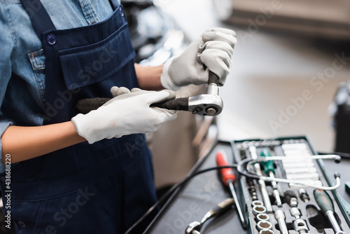 close up view of mechanic hands in gloves holding repairing equipment near toolbox in garage