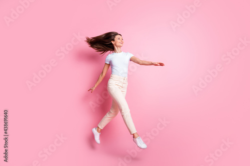 Full size profile photo of optimistic nice brunette hair lady run look empty space wear t-shirt pants isolated on pink background