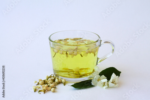 glass cup with herbal hot jasmine tea with bloom flowers of jasmine isolated on white background. healthy drink in mug with dried leaves on the table. copy space.